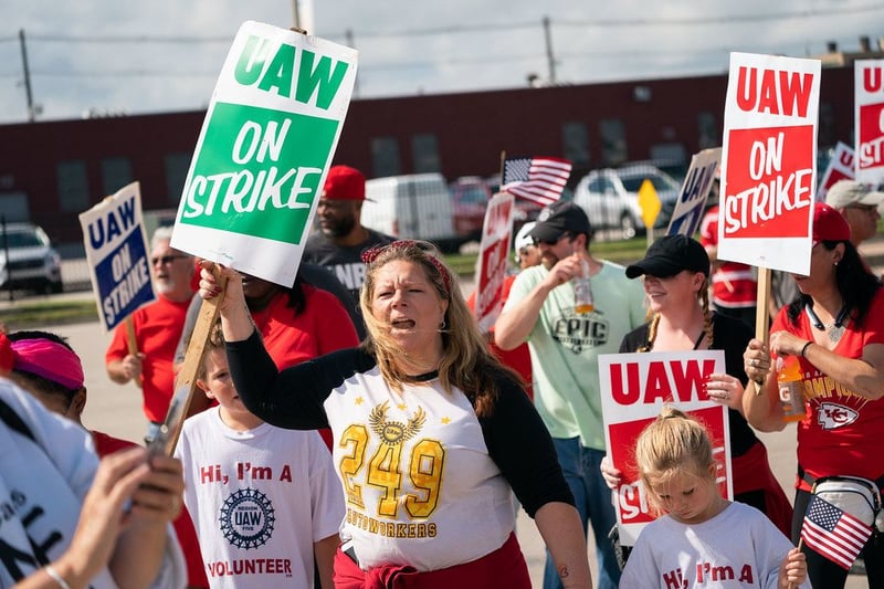 A crowd of people carrying "UAW on strike" picketing signs