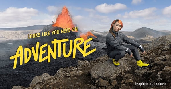 Hip hiker posing on a rock with an exploding volcano in the background, overlaid by text reading "Looks like you need an Adventure" and a footnote of "Inspired by Iceland"