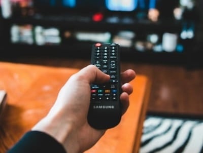 A hand holding a remote pointing to a TV